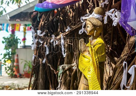 A Wooden Statue Of A Praying Or Meditation Spirit Of Trees, Girl. Tree With White Ribbons. Thai Gree