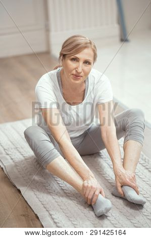 European Looking Woman Over 50 Years Old Doing Yoga At Home In The Living Room. She Sits On The Floo