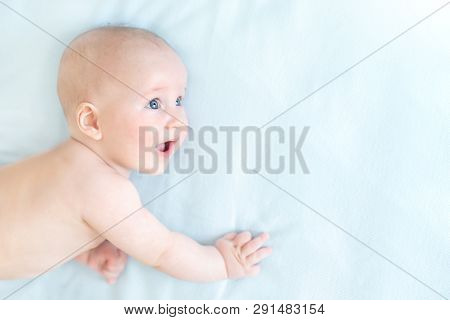 Profile Portrait Of Cute Little Baby Boy Lying On Blue Blanket And Looking Aside. Child With Open Mo