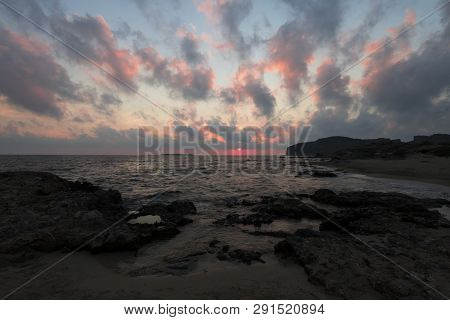 Pink And Blue Sunset On The Beach In Creta, Greece. Beach With Blacks Rocks And Waves At Dusk