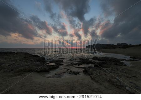Pink And Blue Sunset On The Beach In Creta, Greece. Beach With Blacks Rocks And Waves At Dusk