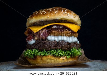 Cheeseburger With Bacon, Lettuce, Cheddar, Onion Rings And Mayonnaise On A Wooden Table