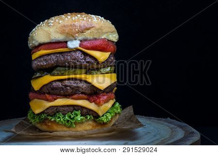 Triple Cheeseburger With Tomato, Lettuce, Pickles And Mayonnaise On A Wooden Table