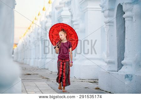 Young girl with traditional burmese umbrella at beautiful white Kuthodaw Pagoda in Mandalay Myanmar
