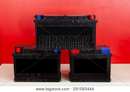 Three New Black Rechargeable Batteries Stand Pyramid On Each Other On A Red Background With White In