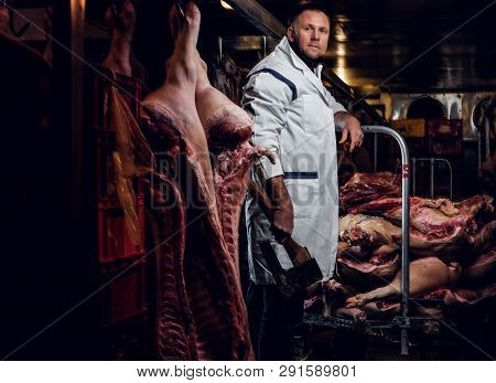 The Butcher In A White Work Shirt Holding Ax While Standing In A Refrigerated Warehouse In The Midst