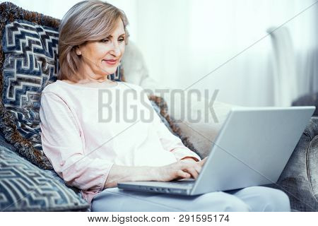 Woman Over 50 Years Old Sits At A Laptop At Home. She Writes A Letter To Her Daughter. The Woman Has
