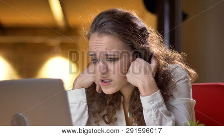Portrait Of Concentrated Young Businesswoman Watching Into Laptop In Puzzlement On Office Background