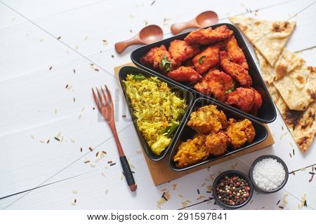 Spicy indian fried chicken served with curry vegetable rice, onion bhajia, naan bread. Placed on white wooden table.