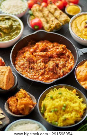 Various Indian dishes on a table. Spicy chicken Tikka Masala in iron pan. Served with rice, naan and spices. Set of different kind Indian food.