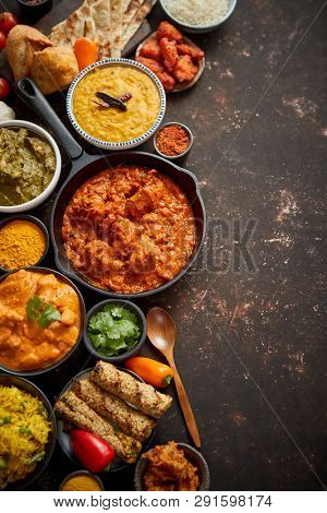 Assortment of various kinds of Indian cousine on dark rusty table. Chicken Tikka Masala, Butter, Nilgiri, Daal Tarka. Served with fried rice, naan bread and spices. Flat lay with copy space.