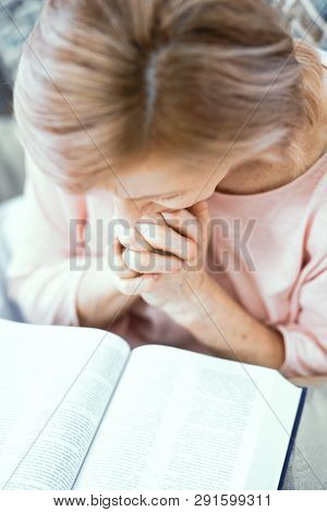 A Woman In Old Age Reads The Bible. Hands Folded In Front Of Her. She Is Praying. Close Up Shot.
