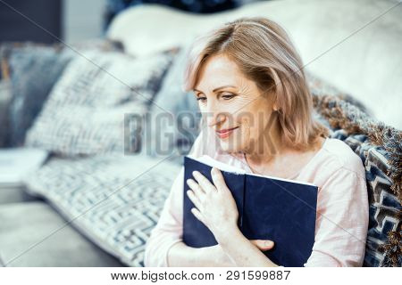 Middle Aged Woman Sitting On Sofa And Holding Bible. Thinking About Soul. Religion Concept.