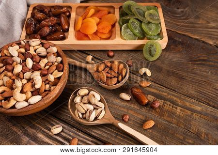 Dates, Dried Apricots And Kiwis In A Compartmental Dish And Assortment Of Nuts In Wooden Bowl On A D