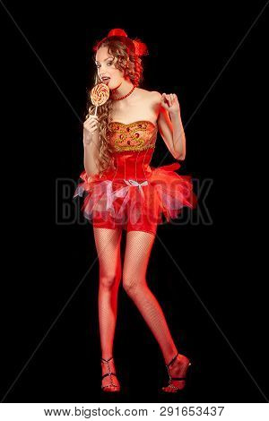Sexy burlesque dancer stripper posing with sweet lollipop, in red corset and red hat with curly hair