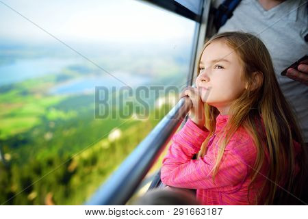 Cute Little Girl Having A Cableway Ride To Tegelberg Mountain, A Part Of Ammergau Alps, Located Nead