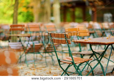 Empty Outdoor Cafe On Autumn Day In Munich, Germany. Empty Chiars And Tables Under Chestnut Trees In
