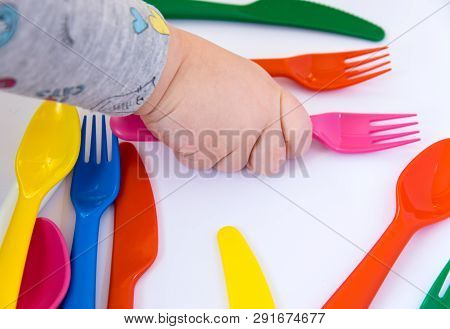 Plastic Red Fork In Hand Of The Small Child. Colorful Tableware On The White Background.