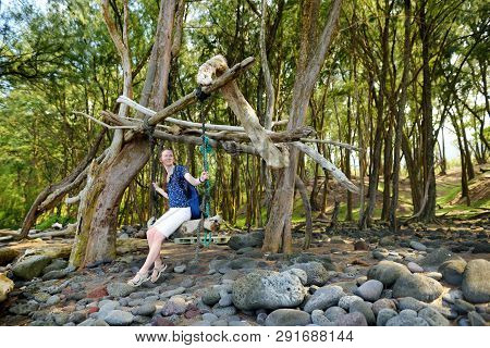 Young Female Tourist Relaxing On A Handmade Swing On Rocky Beach Of Pololu Valley On Big Island Of H