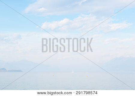 Desenzano del Garda, Italy. Calm beautiful view of italian lake Garda. Amazing landscape in fog with water, sky and mountains. Panorama of gorgeous Lake Garda surrounded by mountains. Heaven on Earth.