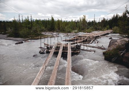 Old, Broken, Wooden Bridge Over The River In The Altai Mountains. Extreme Crossing The River