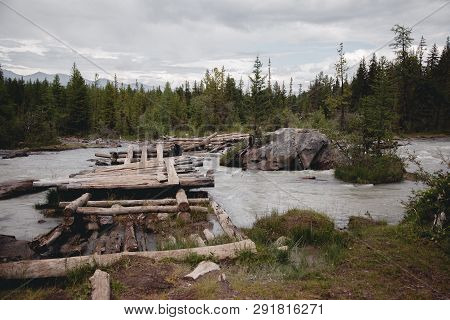 Old, Broken, Wooden Bridge Over The River In The Altai Mountains. Extreme Crossing The River