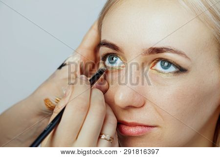 Visagiste With A Brush In One Hand Putting Makeup On The Eyes Of The Model, The Other Hand Pulls The