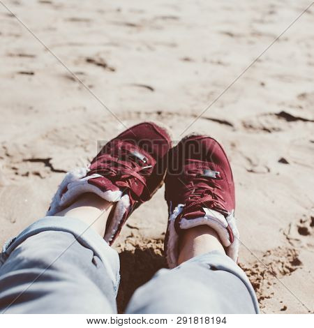 Feet Of Young Woman In Sport Footwear And Jeans Relaxing After Hiking On Sand Beach. Square Pov. Adv