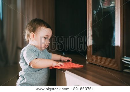 A Little Girl With A Rag Wiping The Dust From The Cabinet