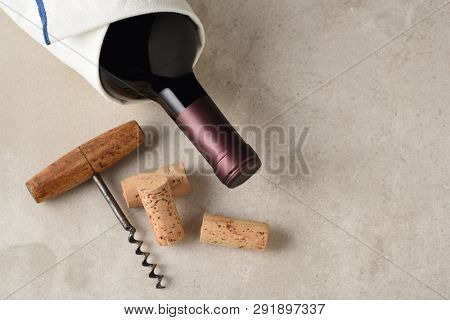 Cabernet Sauvignon Bottle Still Life: A bottle of red wine wrapped in a towel on a gray tile surface the antique cork screw and corks.