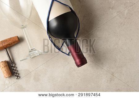 High angle view of a Cabernet Sauvignon wine bottle wrapped in a towel  with wineglass and corkscrew on a gray mottled background - horizontal with copy space