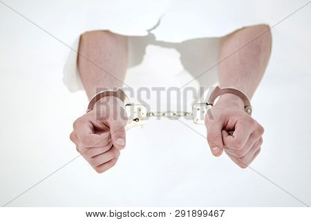Handcuffs on the hands of a man breaking a paper wall