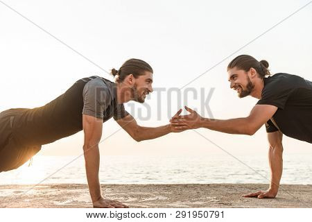 Two twin brothers doing exercises at the beach together, doing push-ups, high five