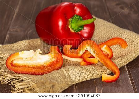 Group Of One Whole Four Slices Of Bulgarian Red Bell Pepper On Jute Cloth On Brown Wood