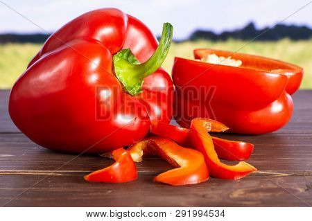 Group Of One Whole One Half Four Slices Of Bulgarian Red Bell Pepper With Green Wheat Field In Backg