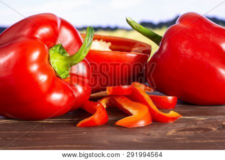 Group Of Two Whole One Half Four Slices Of Bulgarian Red Bell Pepper With Green Wheat Field In Backg