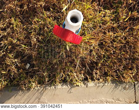 Plastic Pvc Pipe With Red Valve Is Set In Dry Grass Near Curbstone, Water Shortage, Drought