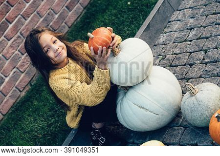 Funny Child Girl In Orange Pullover For Halloween With Pumpkin And On A Dark Brick Background.