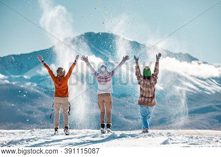 Three Happy Adult Girls Are Having Fun And Throws First Snow On Background Of Mountains. Travel In W