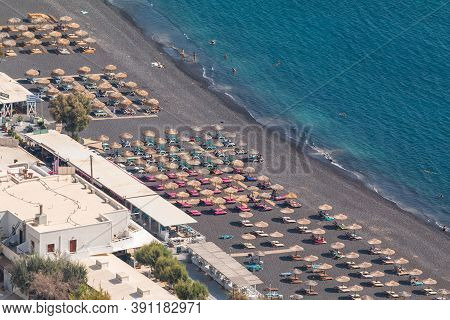 Kamari, Santorini Island, Greece- 19 September 2020: Black, Volcanic Beach Wit Chairs Lawn In Kamari