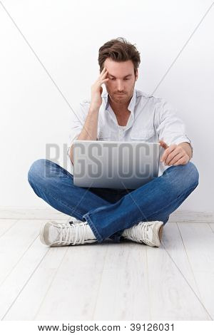 Ung mand sidder i skrædder sæde, browsing internettet på gulvet.