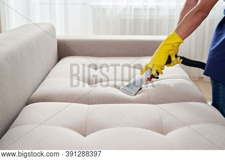 Close-up Of Housekeeper Holding Modern Washing Vacuum Cleaner And Cleaning Dirty Sofa With Professio