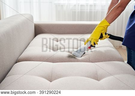 Close-up Of Housekeeper Holding Modern Washing Vacuum Cleaner And Cleaning Dirty Sofa With Professio