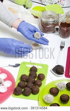 A Woman In Rubber Gloves Makes Candies From Dried Fruits And Nuts. Some Are Sprinkled With Sesame Se