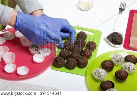 A Woman In Rubber Gloves Makes Candies From Dried Fruits And Nuts. Some Are Sprinkled With Sesame Se