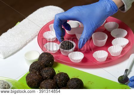 A Woman In Rubber Gloves Makes Candies From Dried Fruits And Nuts. Some Are Sprinkled With Sesame Se