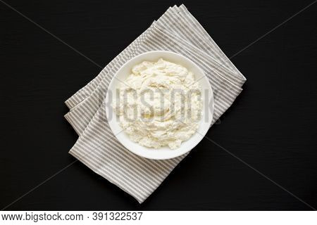 Tasty Ricotta Cheese In A White Bowl On A Black Surface, Top View. Overhead, From Above, Flat Lay.