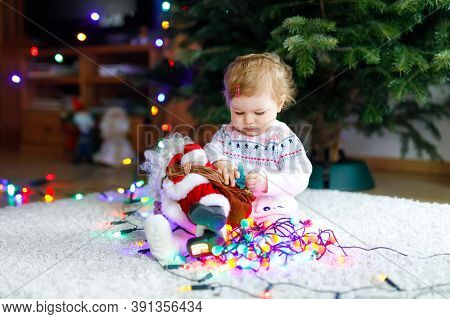 Adorable Baby Girl Holding Colorful Lights Garland In Cute Hands. Little Child In Festive Clothes De