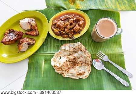 Overhead View Of Roti Canai Or Paratha Served On Banana Leaf, With Mutton Curry And Fried Chicken