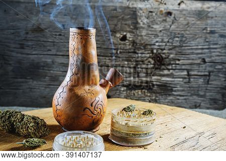 Old Brown Steamung Bong And Open Cannabis Grinder With Chopped Marijuana Weed And Medical Cannabis I